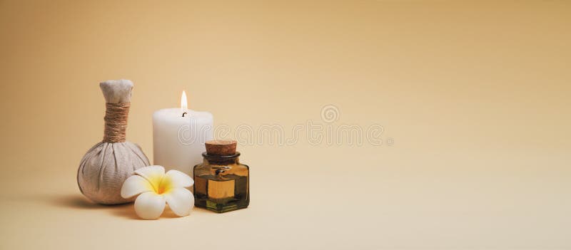 Beautiful spa composition with candle, frangipani flower, oil flask and herbal ball on beige background.