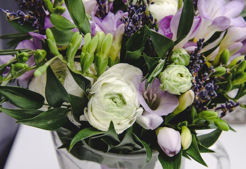 Beautiful spring bouquet of wedding flowers buttercup ranunculus, fresia, lavender in vase with violet tape. Pastel