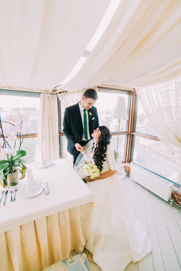 Beautiful stylish pair of newlyweds sharing loving stares in luxurious restaurant interior stock image Beautiful stylish pair of newlyweds sharing loving stares in luxurious restaurant interior stock image