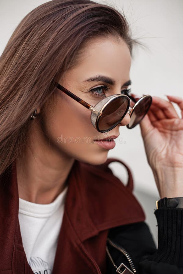 Beautiful stylish portrait young woman in fashionable wear with glasses outdoors in the city. Attractive hipster girl takes off