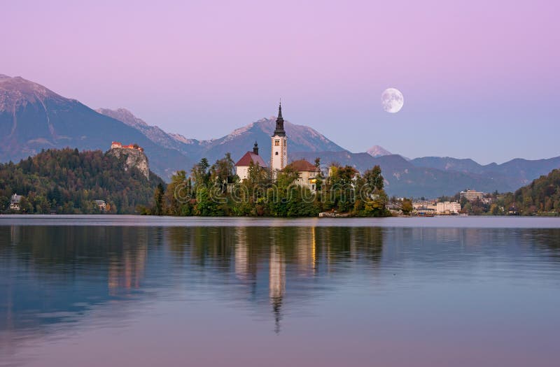 Beautiful sunrise landscape of famous lake Bled in Slovenia with small church on green island on purple sky with moon and royalty free stock images Beautiful sunrise landscape of famous lake Bled in Slovenia with small church on green island on purple sky with moon and royalty free stock images