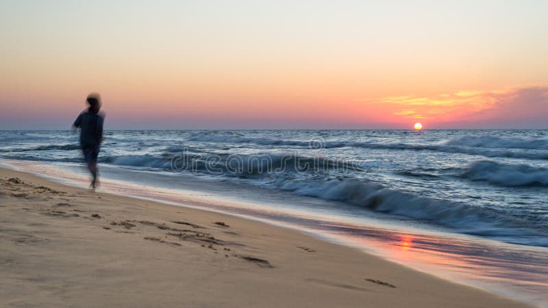 Beautiful sunset at the sea with rough waves on a hot, summer evening, visible shadow of a running person. royalty free stock image
