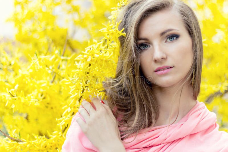 Beautiful sweetheart elegant girl in a pink jacket near shrub with yellow flowers