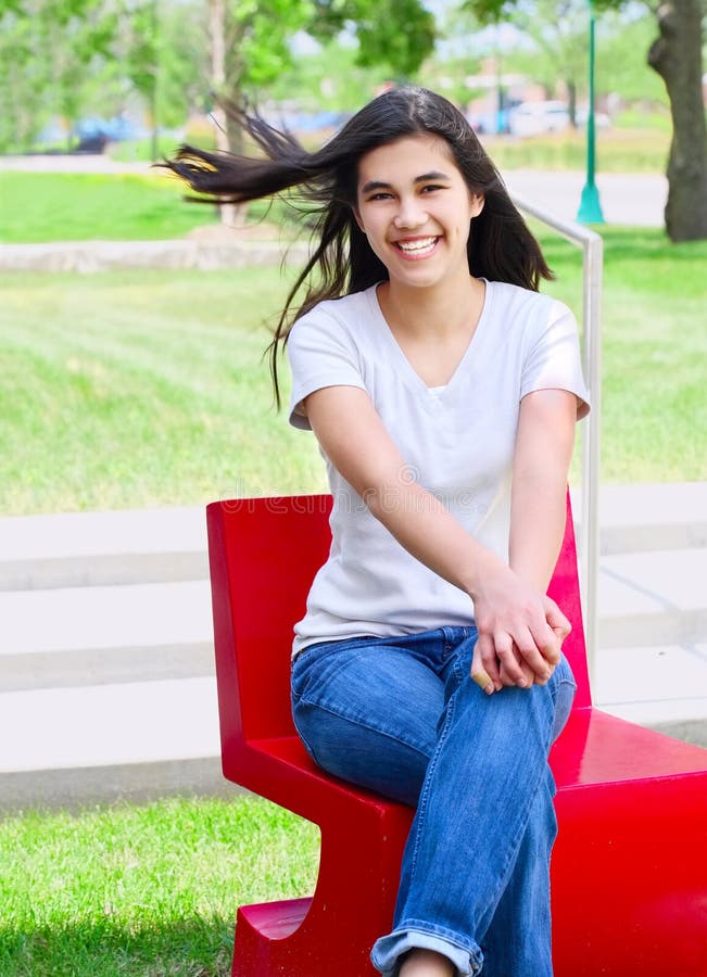 Beautiful teen girl sitting outdoors on red chair