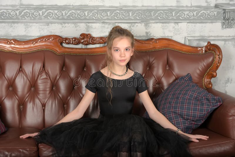 Beautiful teenager girl in black sits on  sofa