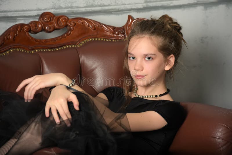 Beautiful teenager girl in black sits on  sofa