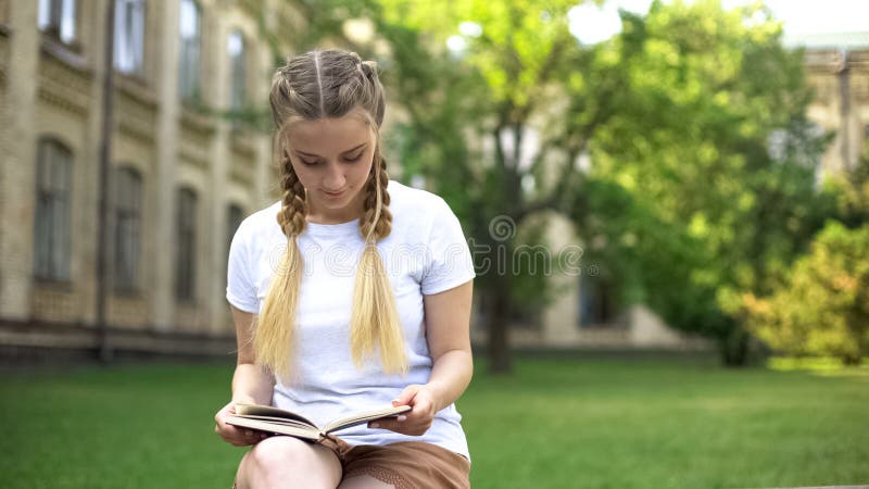 Beautiful teenager girl reading book on bench in campus, preparing homework stock photography Beautiful teenager girl reading book on bench in campus, preparing homework stock photography
