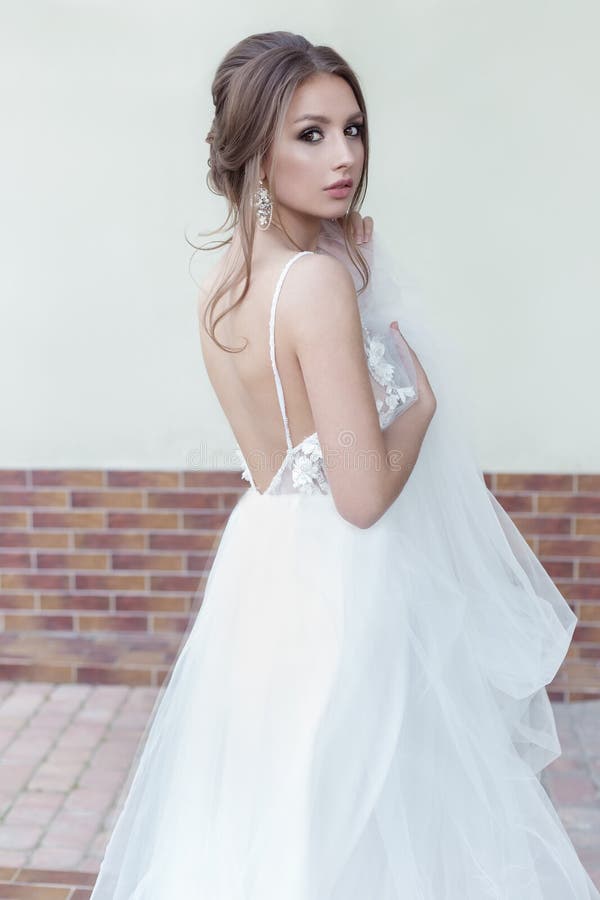 Beautiful tender sweet girl bride with a festive hairdo and light make-up with a veil in her hands with rich costume jewelery earr