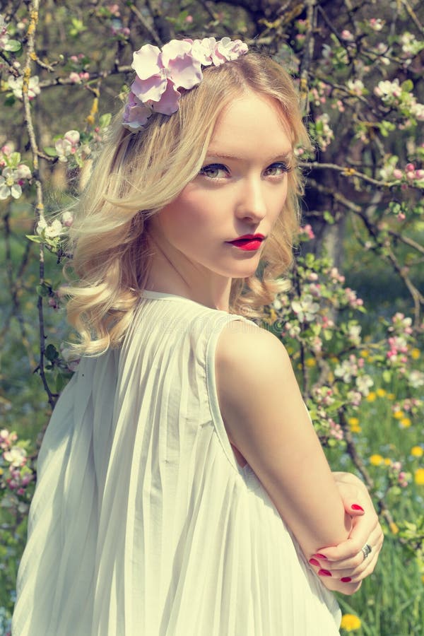 Beautiful tender sweet young girl with a wreath of flowers in her hair in a white light dress walks in the lush garden