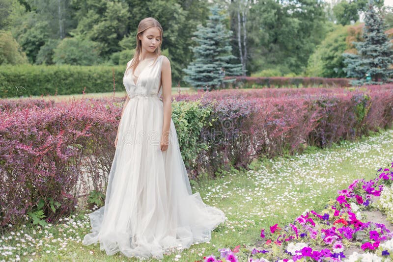 Beautiful tender young woman bride in her wedding dress gentle air walks in the lush garden on a hot sunny summer day