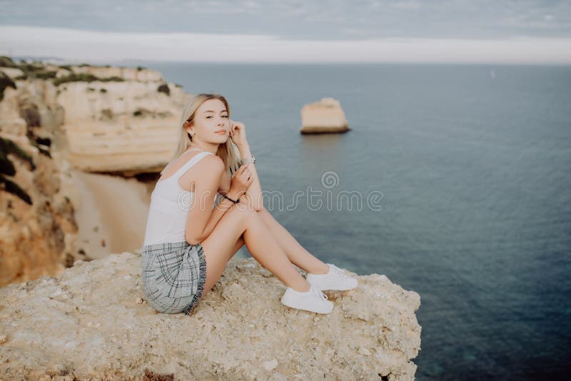 Beautiful thinking woman sitting on the stone on blue ocean and sky background in sunset. Travel concept. royalty free stock image Beautiful thinking woman sitting on the stone on blue ocean and sky background in sunset. Travel concept. royalty free stock image