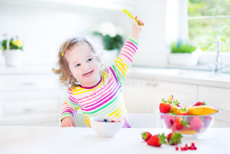 Beautiful toddler girl with curly hair having breakfast