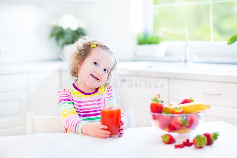 Beautiful toddler girl having breakfast drinking juice