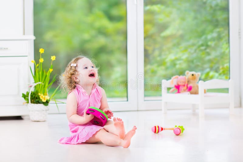 Beautiful toddler girl playing tambourine in white room