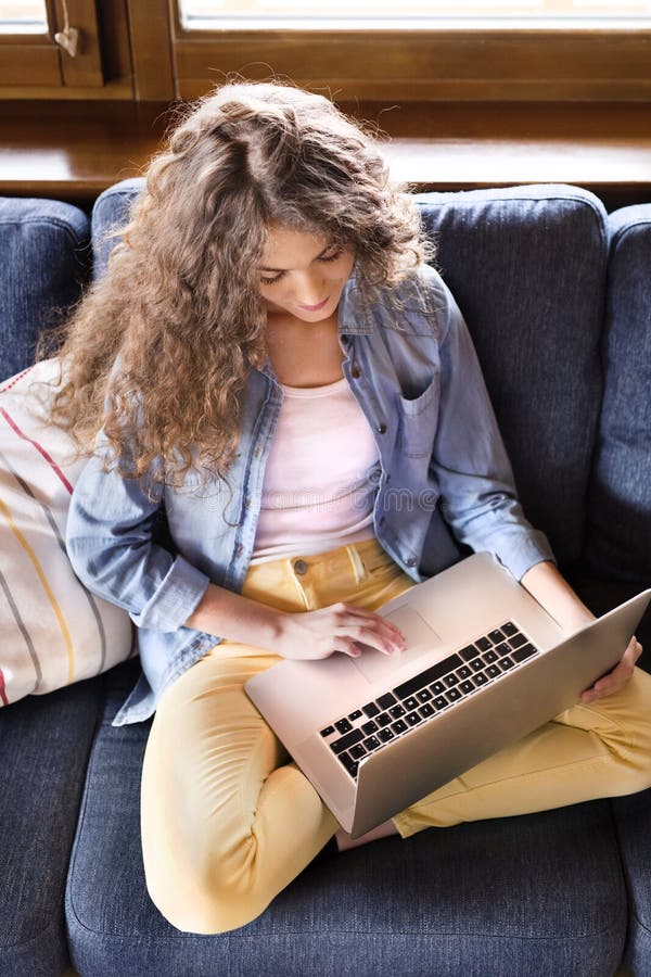 A beautiful university student is writing her thesis on a laptop, sitting at home on the couch. royalty free stock photos