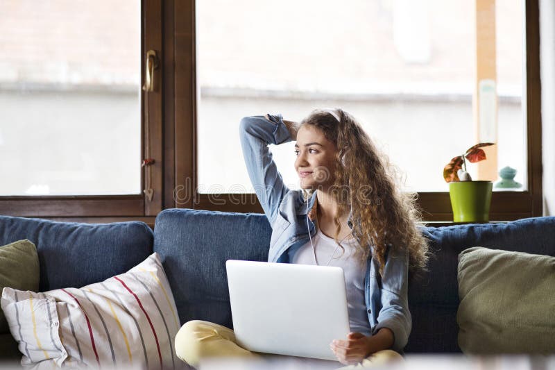 A beautiful university student is writing her thesis on a laptop, sitting at home on the couch. stock photo
