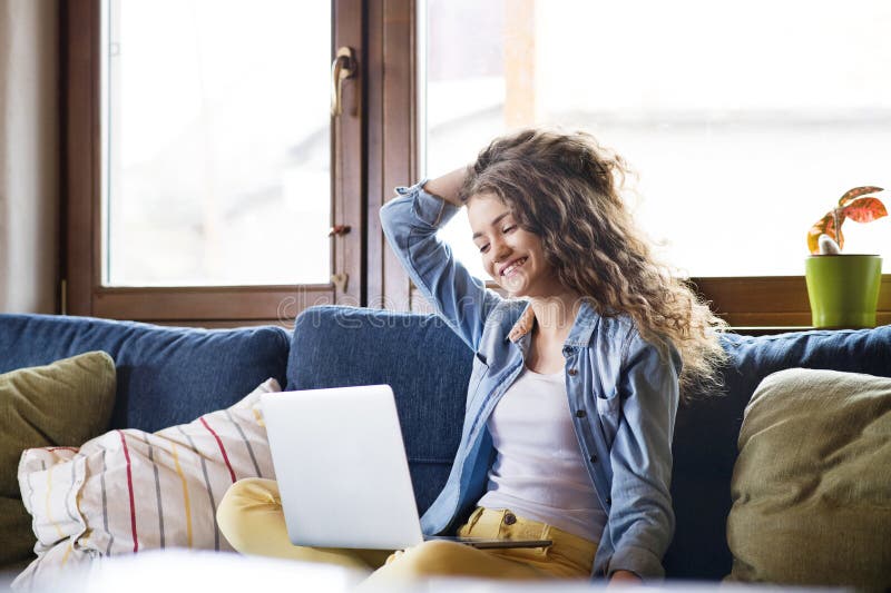 A beautiful university student is writing her thesis on a laptop, sitting at home on the couch. royalty free stock photo