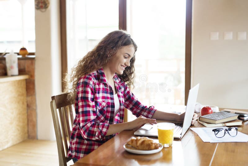A beautiful university student is writing her thesis on a laptop, sitting at home at table. royalty free stock photo