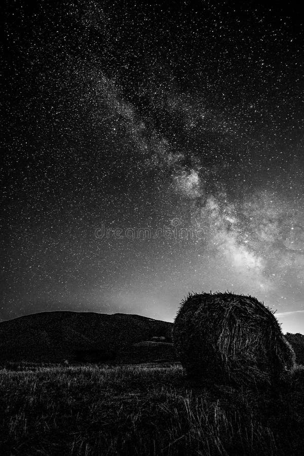 Beautiful view of starred night sky with milky way over a cultivated field with hay bale