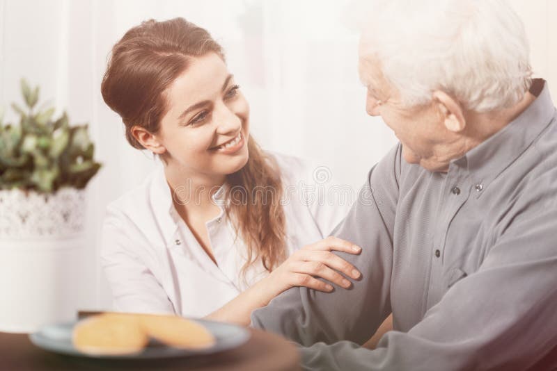 Volunteer smiling at senior man at nursing home stock photo