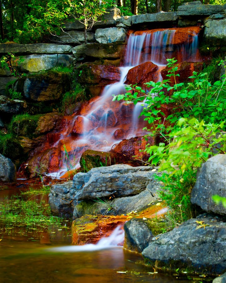 Water cascades over the red algae covered rock of a beautiful man-made waterfall in Andrew Haydon park in Ottawa, Ontario Canada. Man made waterfall stock images, royalty-free photos and pictures
