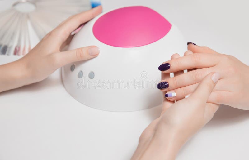 Beautiful well-groomed woman`s hand manicurist holds lamp for gel Polish and demonstrates perfect coverage of his client purple. royalty free stock images Beautiful well-groomed woman`s hand manicurist holds lamp for gel Polish and demonstrates perfect coverage of his client purple. royalty free stock images