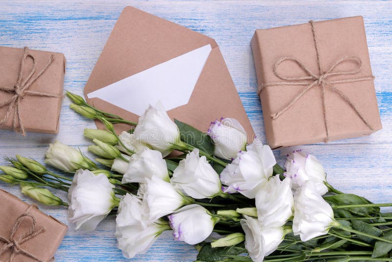 White bouquet of flowers eustoma with gift boxes and an envelope on a blue wooden background stock photography