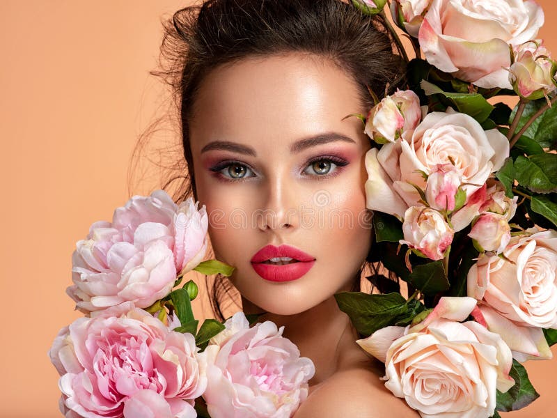 Beautiful white girl with flowers. Stunning brunette girl with big bouquet flowers of roses. Closeup face of young beautiful woman