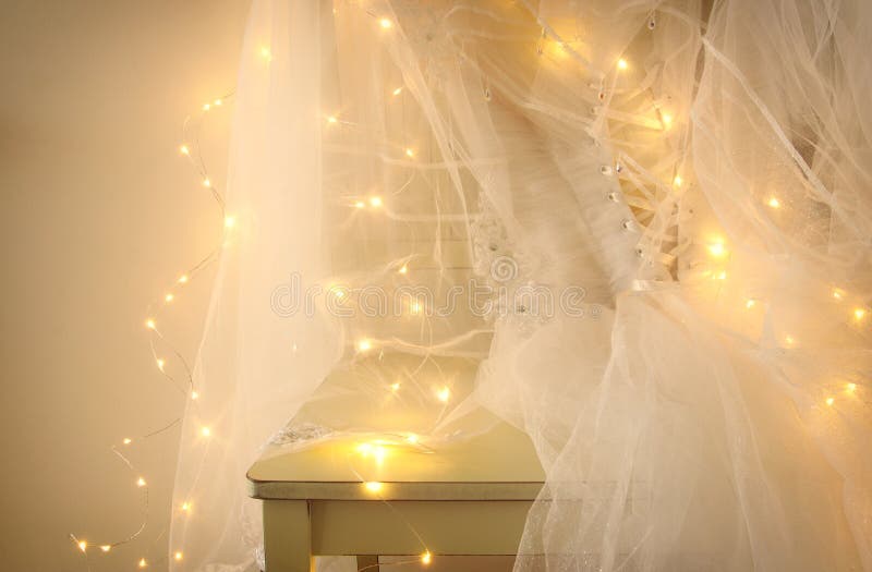 Beautiful white wedding dress and veil on chair with gold garland lights