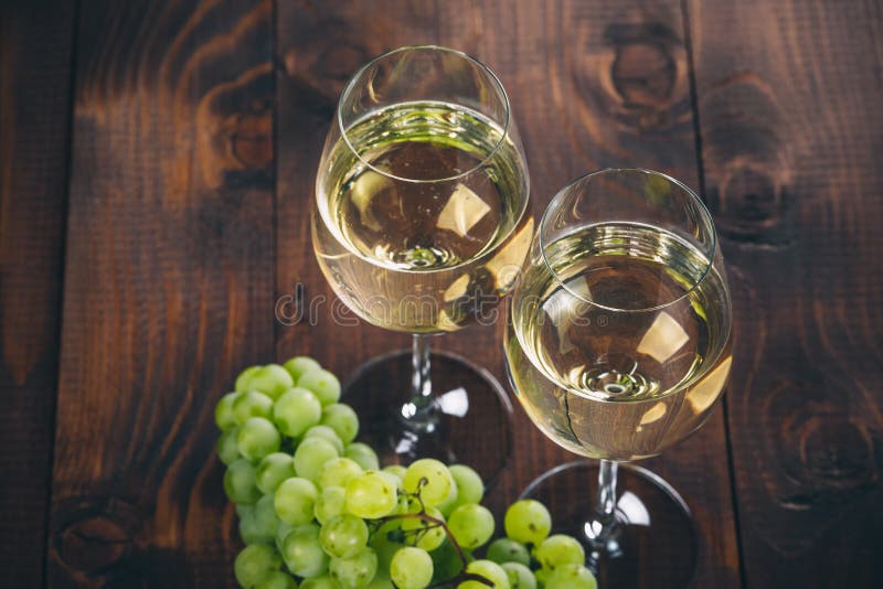 Beautiful White wine in wine glass with a bunch of green grapes, on a wooden background with free space