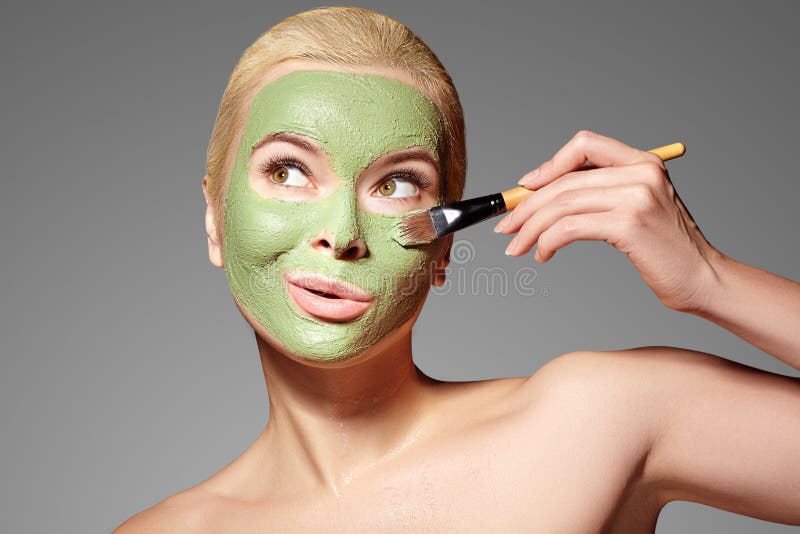 Beautiful Woman Applying Green Facial Mask. Beauty Treatments. Spa Girl Apply Clay Facial mask on grey background