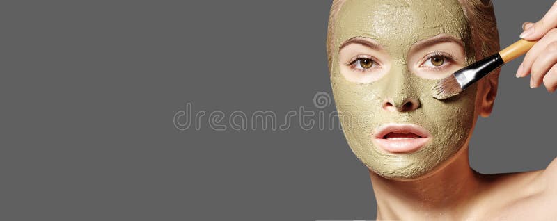 Beautiful Woman Applying Green Facial Mask. Beauty Treatments. Spa Girl Apply Clay Facial mask on grey background