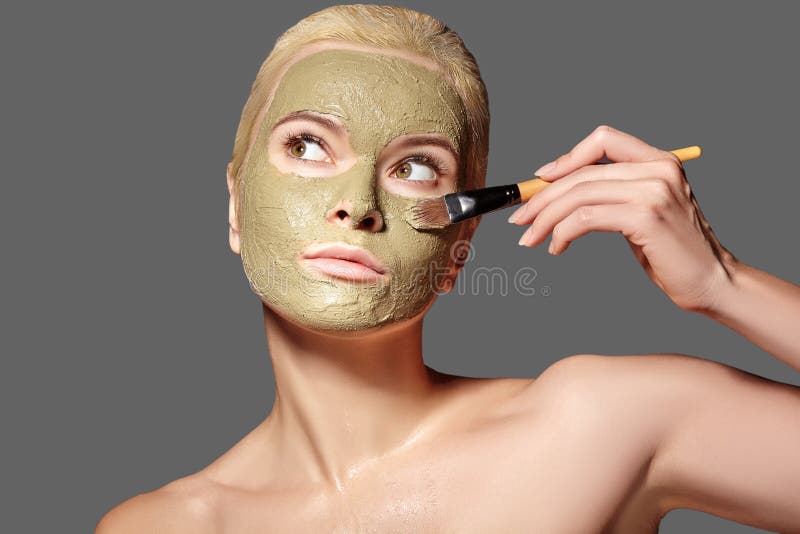 Beautiful Woman Applying Green Facial Mask. Beauty Treatments. Spa Girl Apply Clay Facial mask on grey background