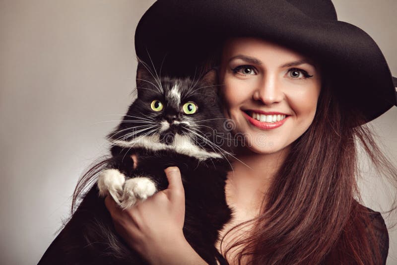 Beautiful woman in black dress and hat with cat