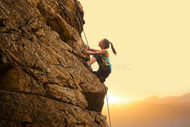 Beautiful Woman Climbing on the Rock at Foggy Sunset in the Mountains. Adventure and Extreme Sport Concept