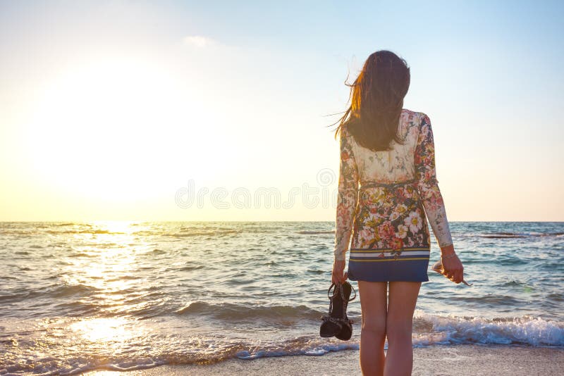 Beautiful woman in colorful dress standing on the beach near the ocean and looking far away at the sunset stock images Beautiful woman in colorful dress standing on the beach near the ocean and looking far away at the sunset stock images