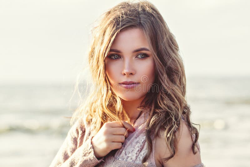 Beautiful woman face closeup portrait. Pretty girl with long curly brown hair on ocean background. Perfect natural beauty