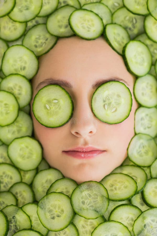 Close up di una giovane e bella donna con maschera facciale di le fette di cetriolo sul viso al salone spa.