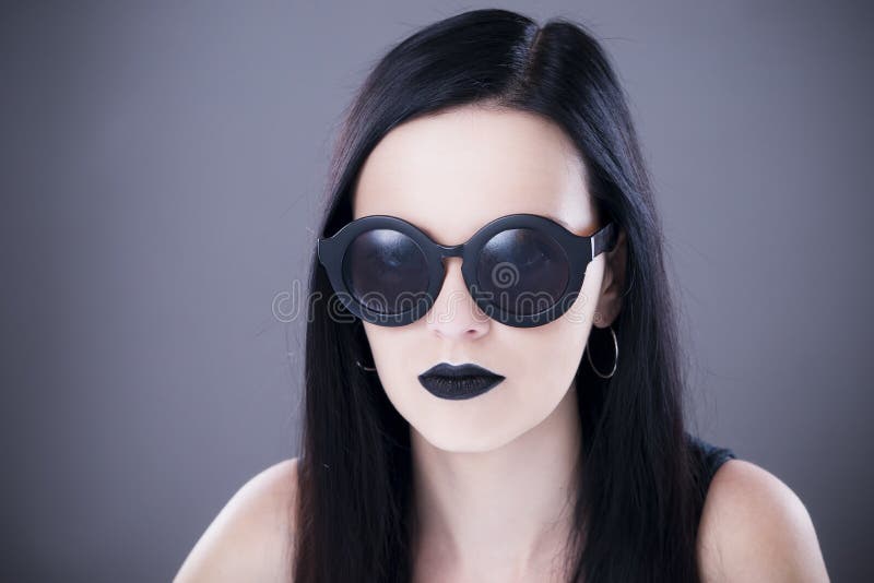 Beautiful woman fashion model portrait in sunglasses with black lips and earrings. Creative hairstyle and make up. Beauty girl on a gray background