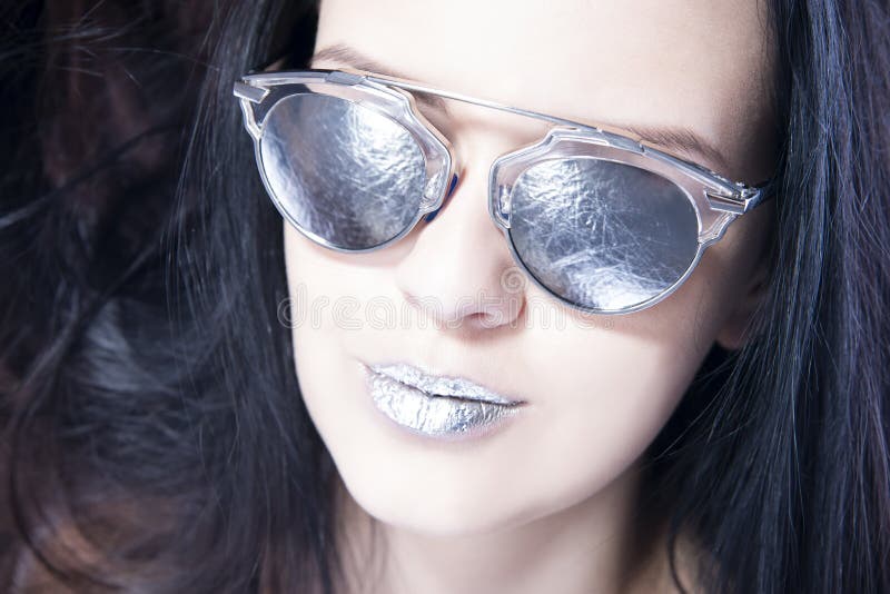 Beautiful woman fashion model portrait in sunglasses with metallic silver lips. Creative hairstyle and make up. Beauty girl close up on a gray background