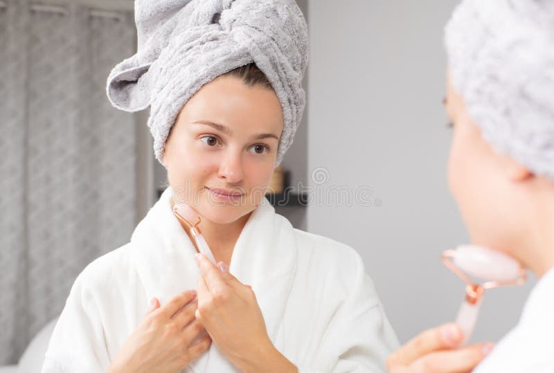 Beautiful Woman Is Getting Massage Face Using Jade Roller In Front Of The Mirror At Home Stock