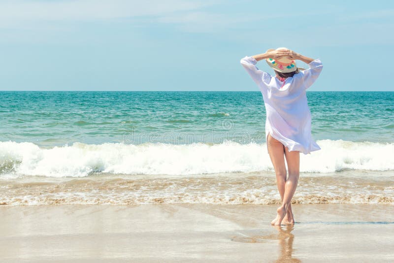 Beautiful woman with hands up relaxing on the sand beach with sea view, enjoying the summer breeze and sound of the waves