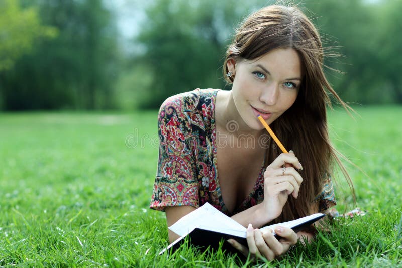 Beautiful woman lays on a grass in park with a diary in ha