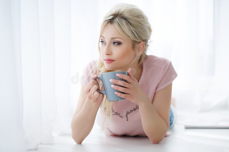 Beautiful woman lying on a white floor with a Cup of tea