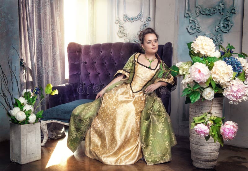 Beautiful young woman in long medieval dress on the sofa. Beautiful young woman in long medieval dress on the sofa
