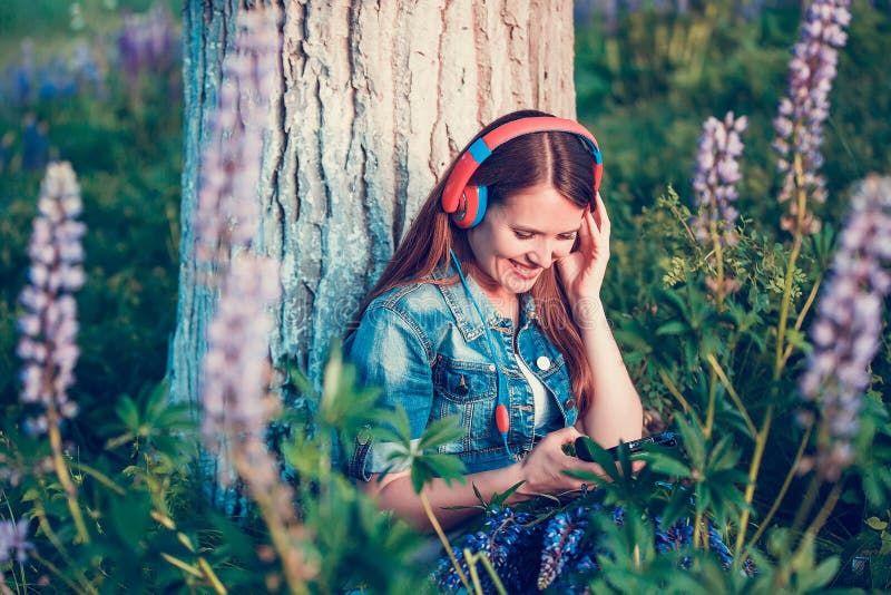 Beautiful woman near the tree and the lupine field is listening to music on headphones and having fun stock photos Beautiful woman near the tree and the lupine field is listening to music on headphones and having fun stock photos