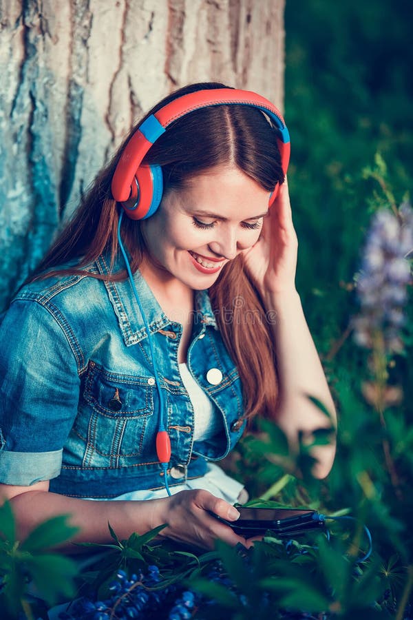 Beautiful woman near the tree and the lupine field is listening to music on headphones and having fun royalty free stock photography Beautiful woman near the tree and the lupine field is listening to music on headphones and having fun royalty free stock photography