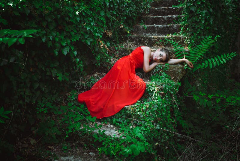 Beautiful woman in red dress lying on the steps of the old stair