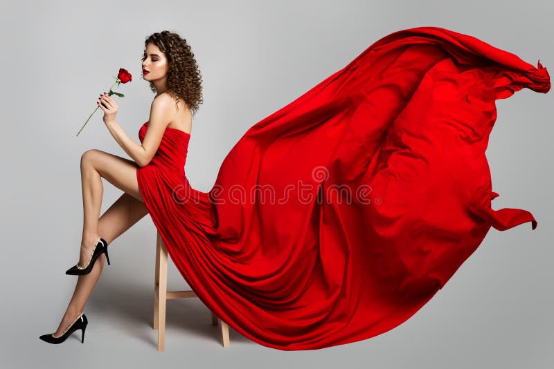 Beautiful Woman in Red Dress Smelling Roses Flowers, Fashion Model Studio Portrait on White, Flying Fluttering Cloth on Wind