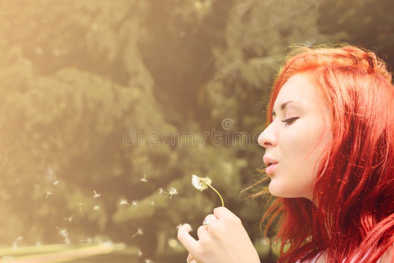 Beautiful woman with red hair blows into dandelion